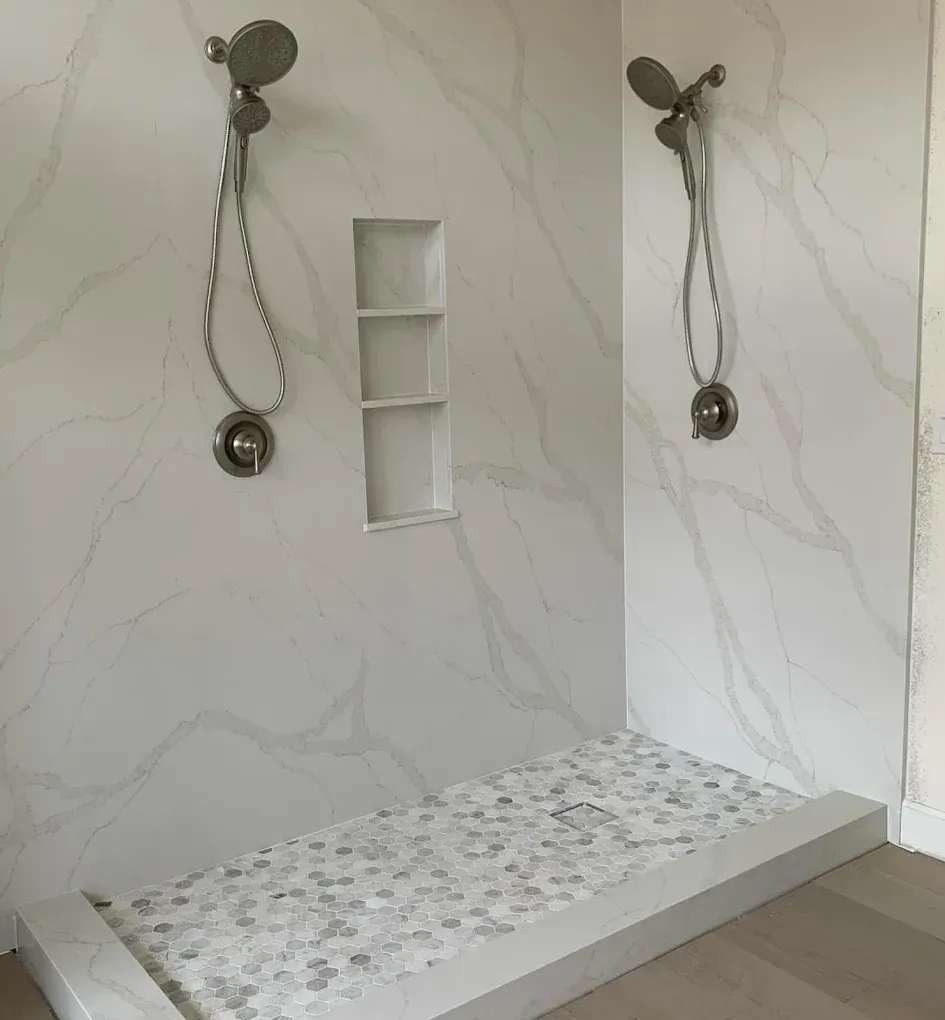 Modern shower with marble-look walls, rainfall heads, built-in niches, and a pebble-tile shower floor.
