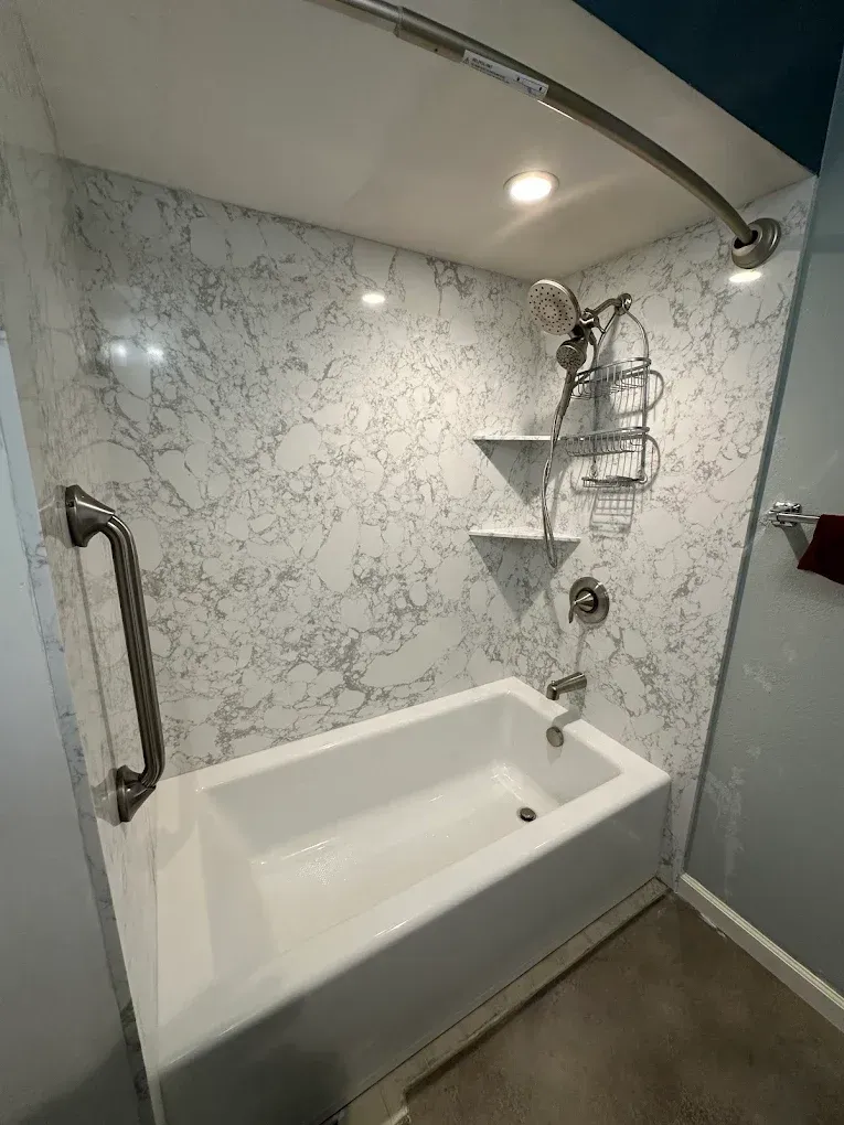 Small accessible bathroom with a walk-in tub, grab bars, marble-look wall, and shower fixtures