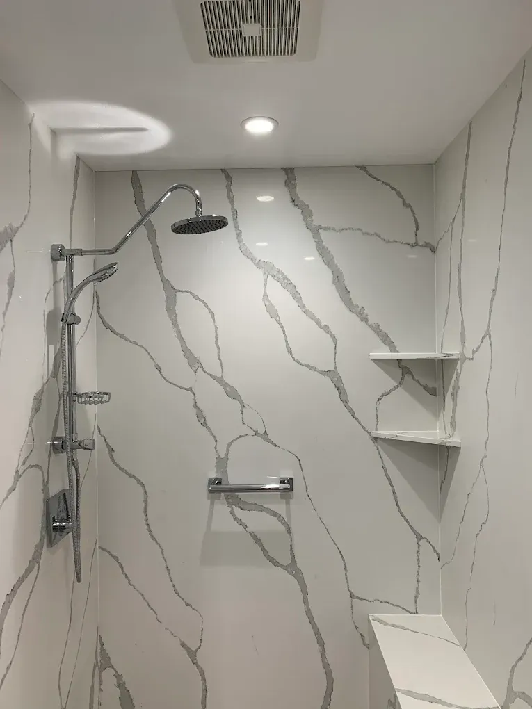 Modern shower with marble-pattern tile, rain showerhead, glass shelf, and built-in bench.
