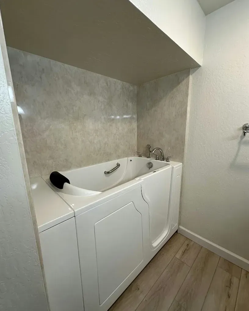 Compact bathroom with a white soaking tub, tiled surround, and wood-look floor