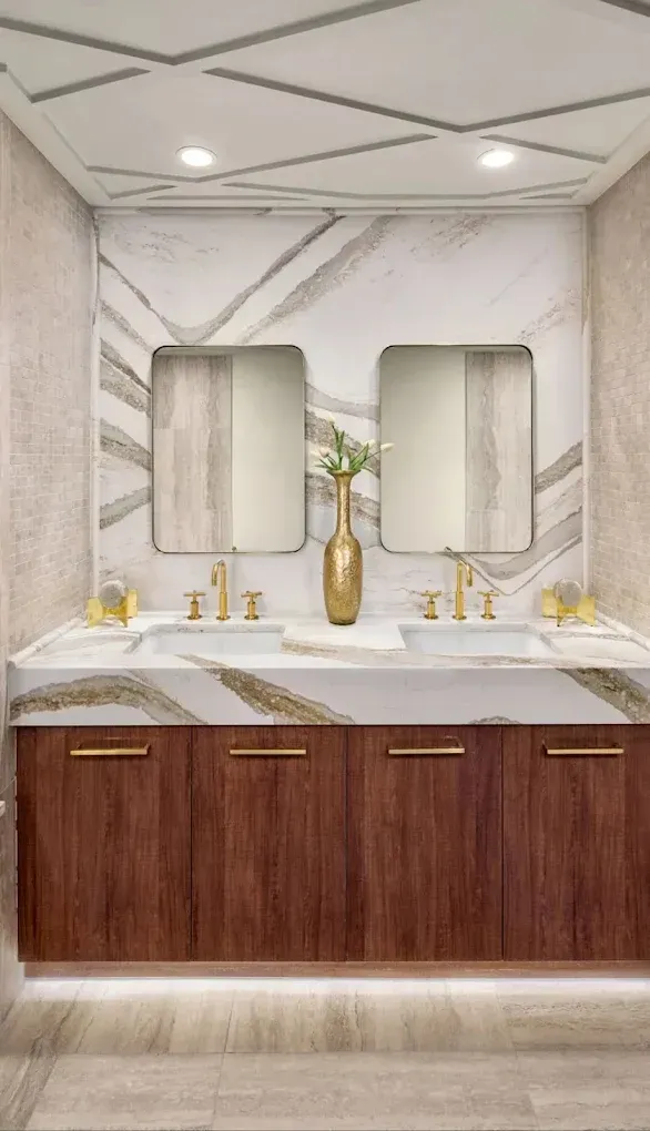 Modern bathroom vanity with marble walls, wood cabinets, gold fixtures, and two mirrors