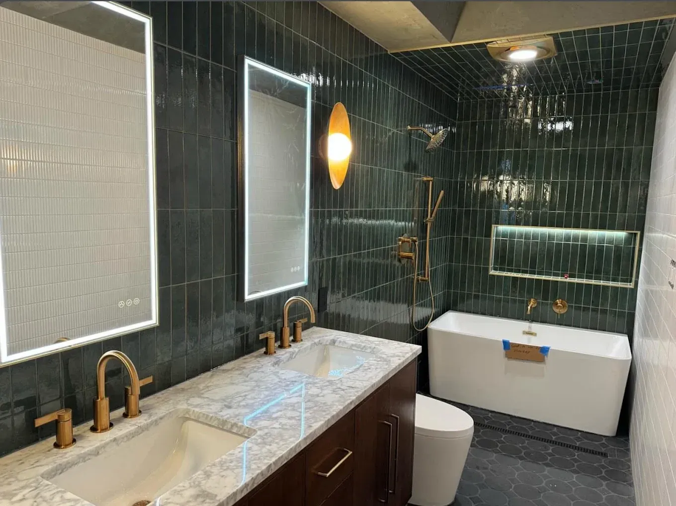 Modern bathroom with marble vanity, black tile walls, pendant light, tub, and toilet