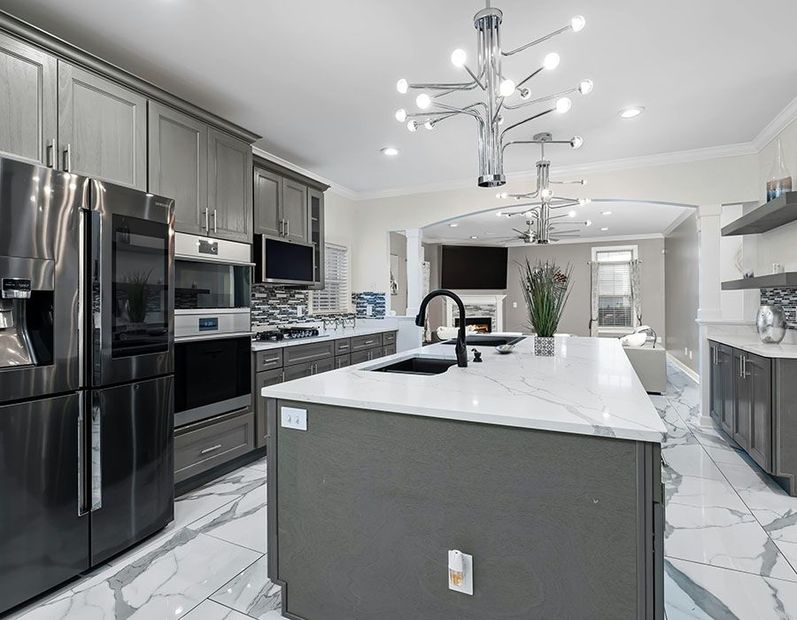 Modern gray kitchen with stainless appliances, white island, marble-look floor, and pendant lights.