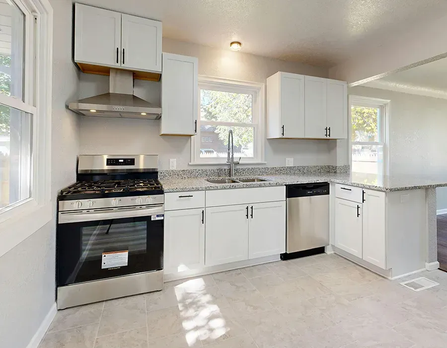 Bright kitchen with white cabinets, black stove, stainless dishwasher, and light countertops near windows.