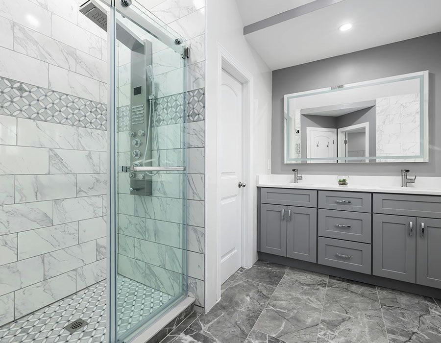Modern bathroom with glass shower, gray vanity, large mirror, and tiled floor.