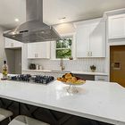 Bright modern kitchen with white cabinets, island, stainless range hood, and a fruit bowl on the counter