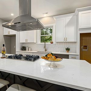 Bright modern kitchen with white cabinets, island, stainless range hood, and a fruit bowl on the counter