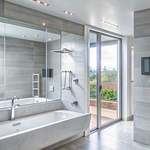 Modern bathroom with a freestanding tub, large mirror, gray tile, and glass door to a balcony