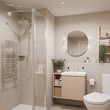 Modern beige bathroom with glass shower, round mirror, vanity, and white toilet