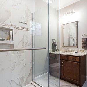 Bright modern bathroom with glass shower, white marble tile, and dark wood vanity