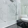 Modern white bathroom with marble walls, glass shower enclosure, and black vanity with sink