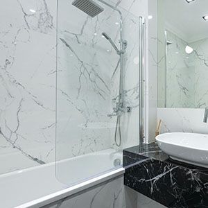 Modern white bathroom with marble walls, glass shower enclosure, and black vanity with sink