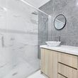 Modern bathroom with glass shower, marble-tile walls, and light wood vanity with vessel sink.
