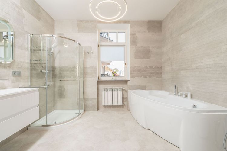 Bright modern bathroom with glass shower, white tub, vanity, and window.