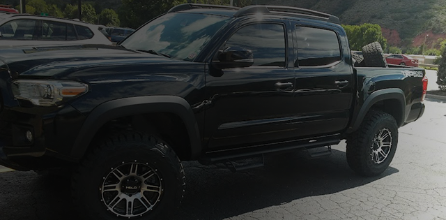 A black Toyota Tacoma pickup truck with aftermarket wheels parked outdoors. | Avon Auto & Truck