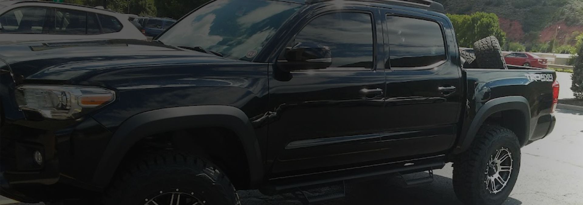 A black Toyota Tacoma pickup truck parked outdoors in a sunlit lot. | Avon Auto & Truck