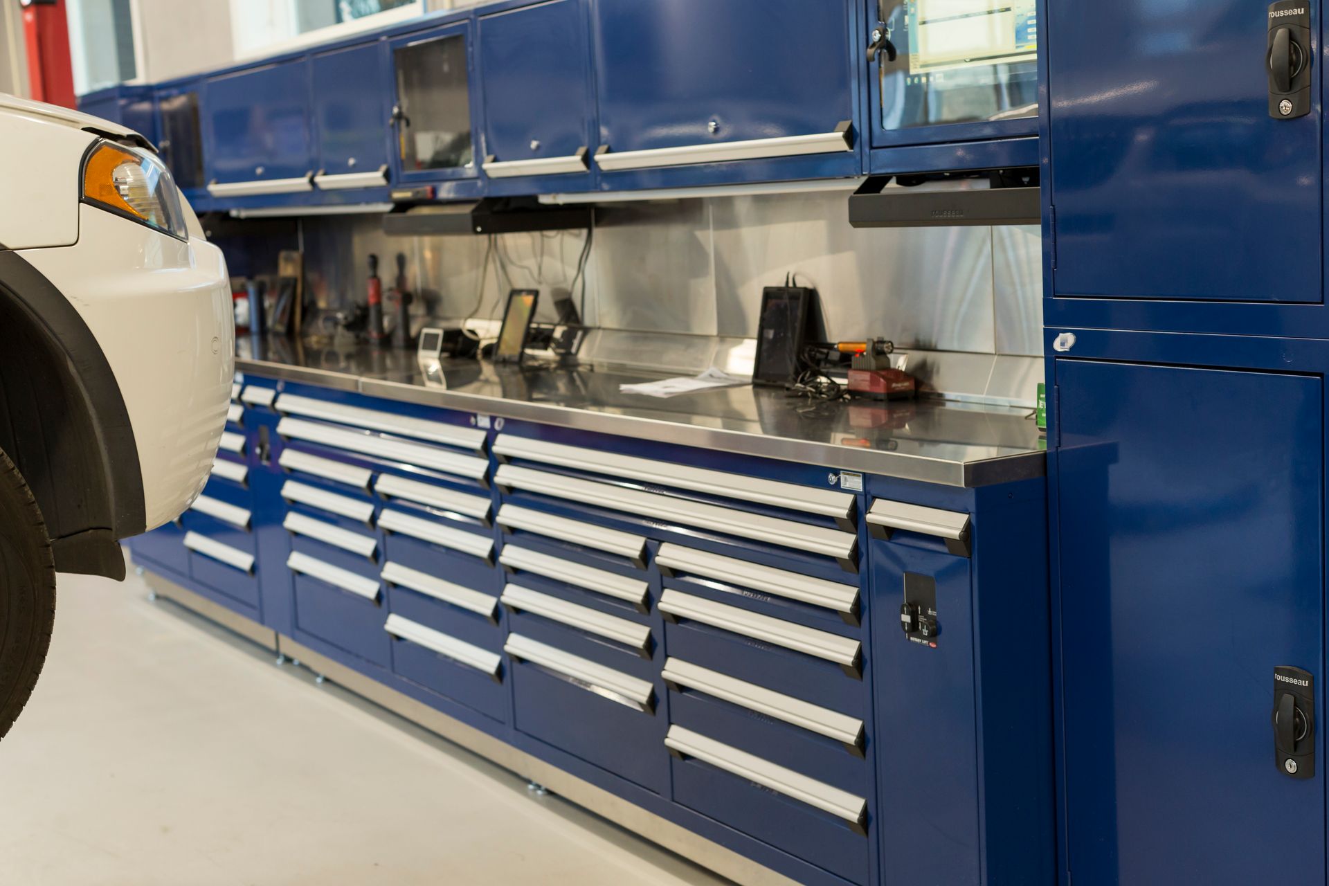 Blue tool cabinets and workspace in a garage, with a car partially visible on the left. | Plandome Service Center