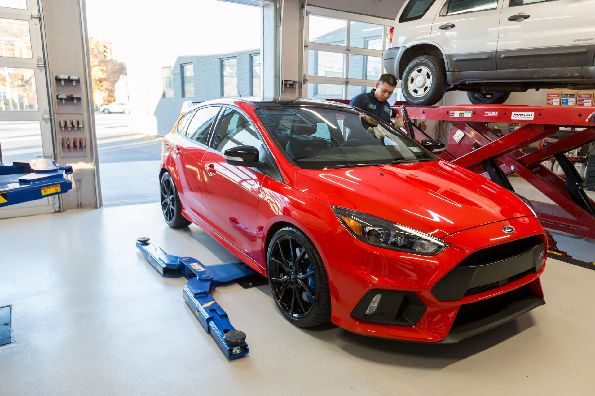 Red Ford Focus RS on a lift in a garage, mechanic working on a white van. | Plandome Service Center