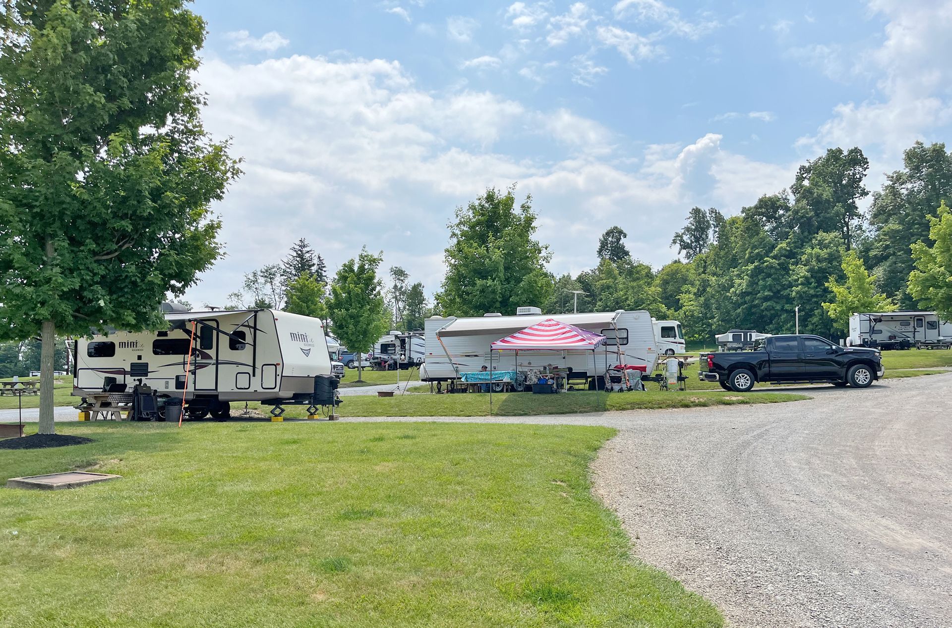 Campground with RVs and cars parked on gravel, sunny day.