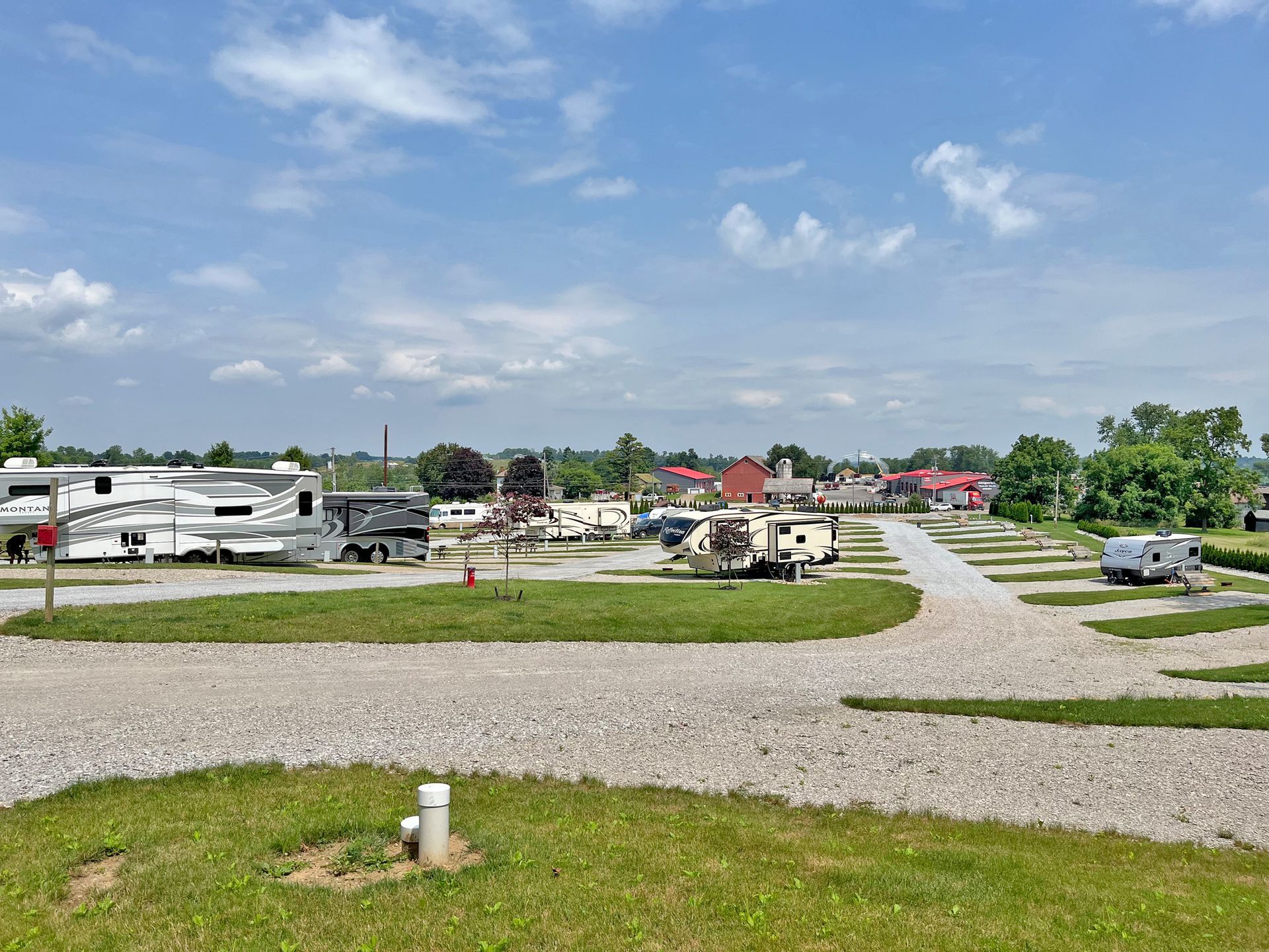 RV park on a sunny day with gravel campsites, recreational vehicles, and a distant town under a blue sky.