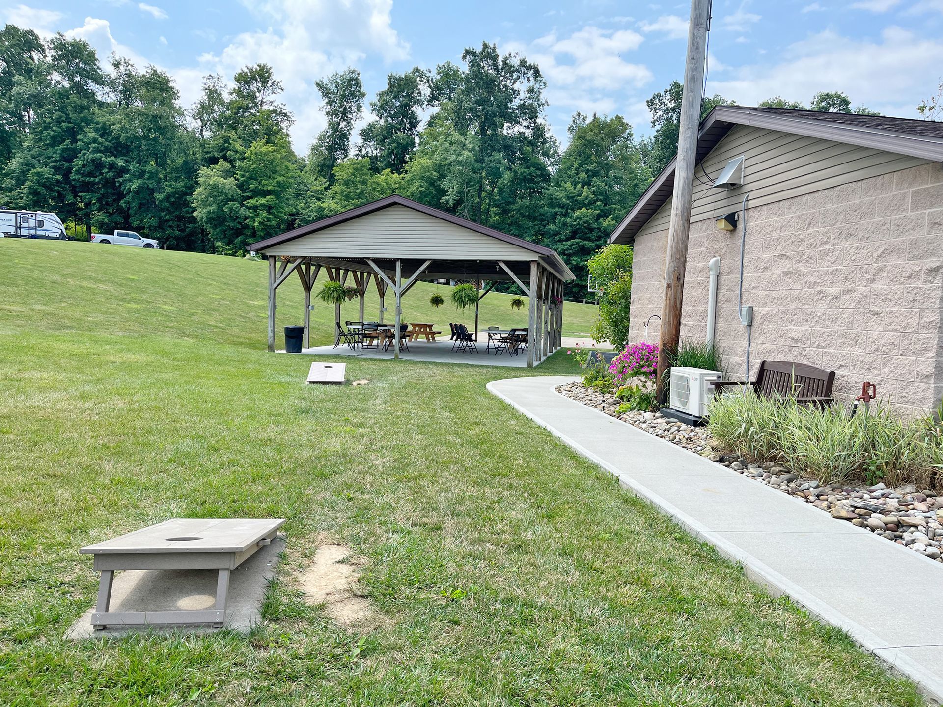 Grassy area with a covered pavilion, building, and a cornhole game.