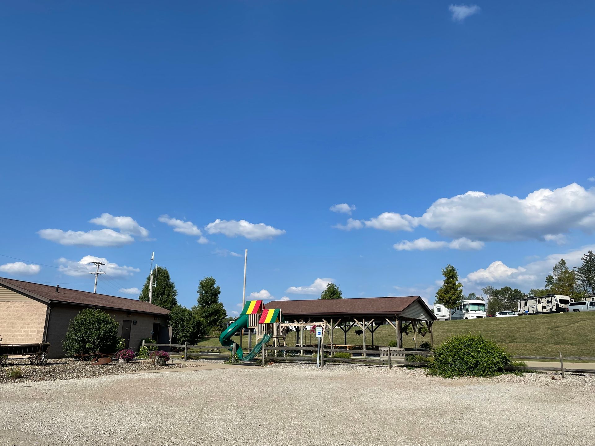Playground with slide, picnic shelter, and building under a blue sky with clouds.