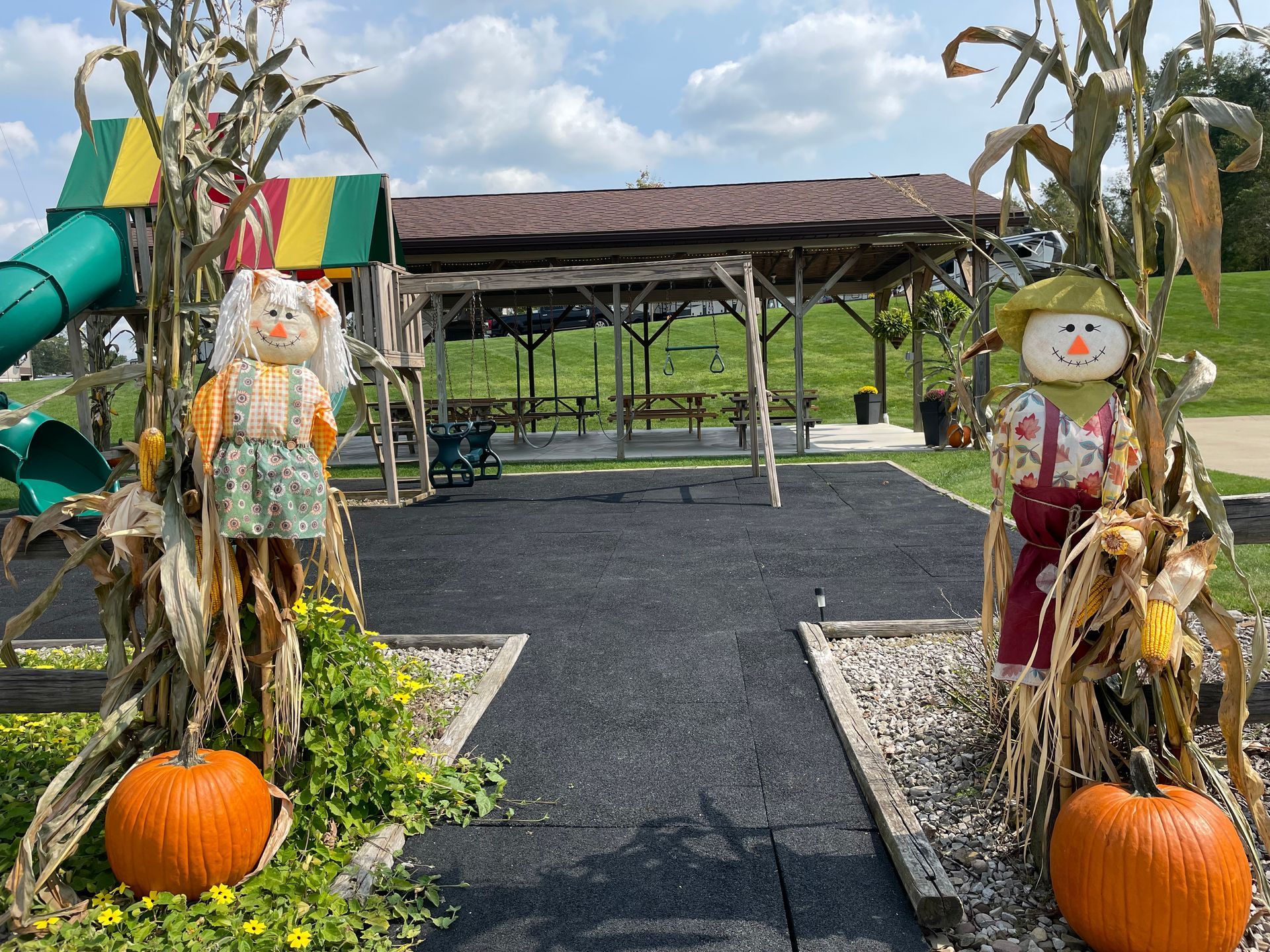 Playground with scarecrows, pumpkins, and a covered picnic area under a bright sky.
