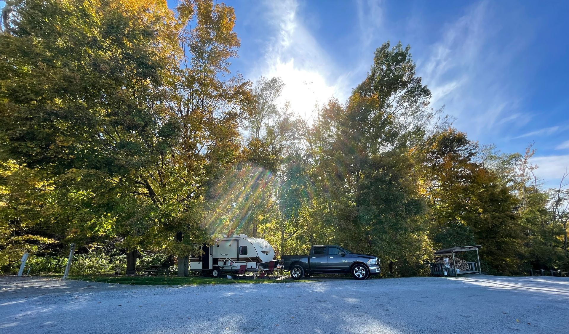 RV and truck parked beneath trees with sun shining through.