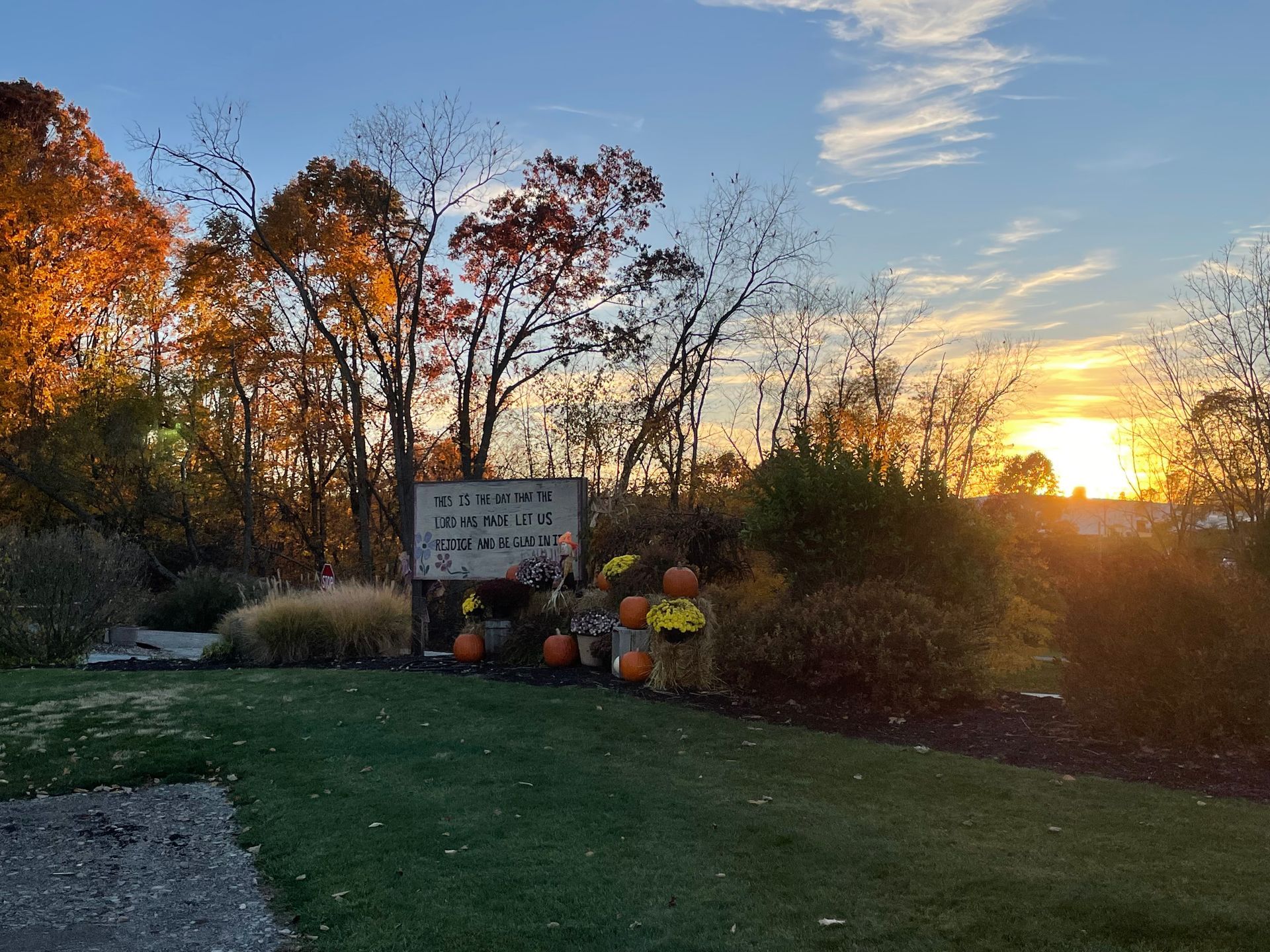 Autumn scene: Fall decorations and sign on green lawn, with trees and sunset in the background.