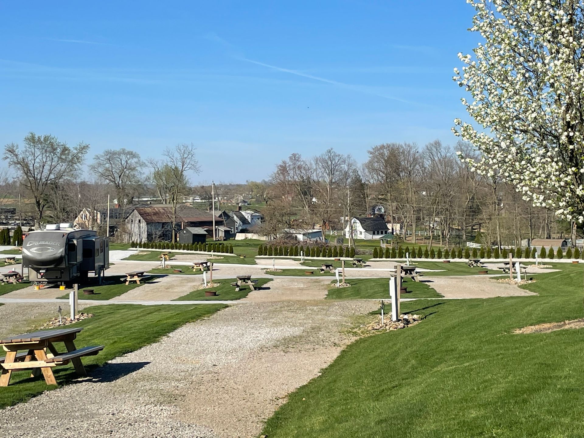 RV park with gravel sites, picnic tables, and a town in the background on a sunny day.