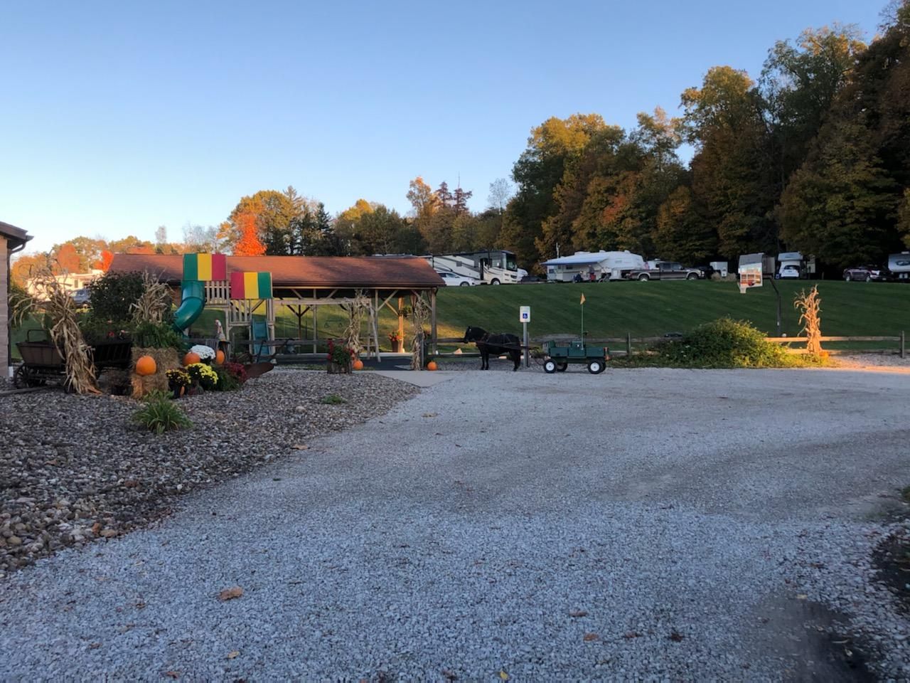 Gravel driveway leads to a campground with a building, decorations, and RVs on a hill.