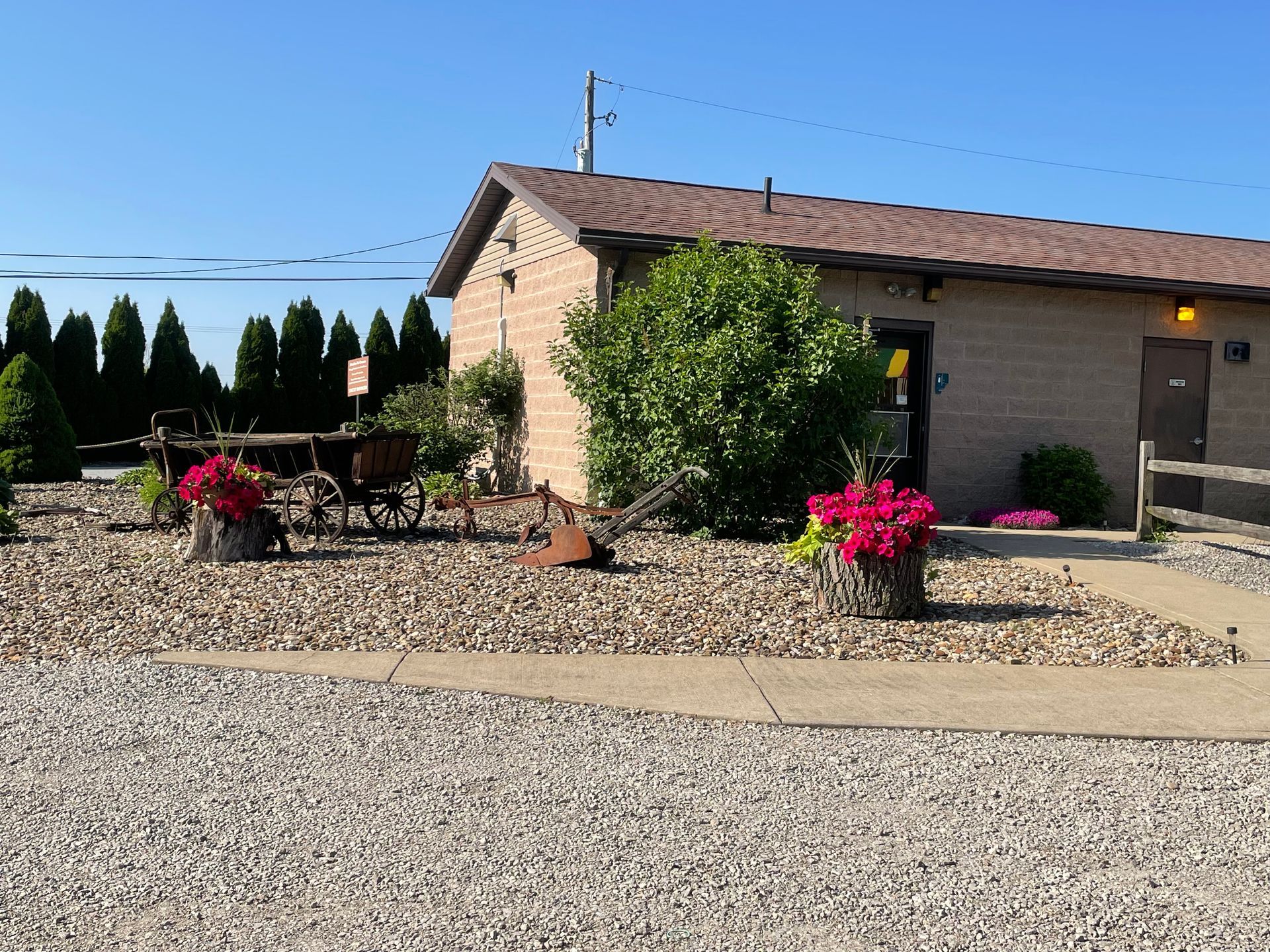 Building with flower pots, gravel landscaping, and an antique cart. Sunny day.