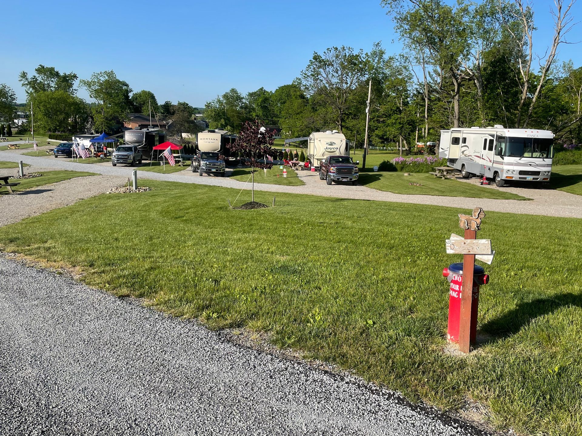 RV campground on a sunny day. RVs parked on grassy sites with gravel roads. Red fire hydrant in foreground.