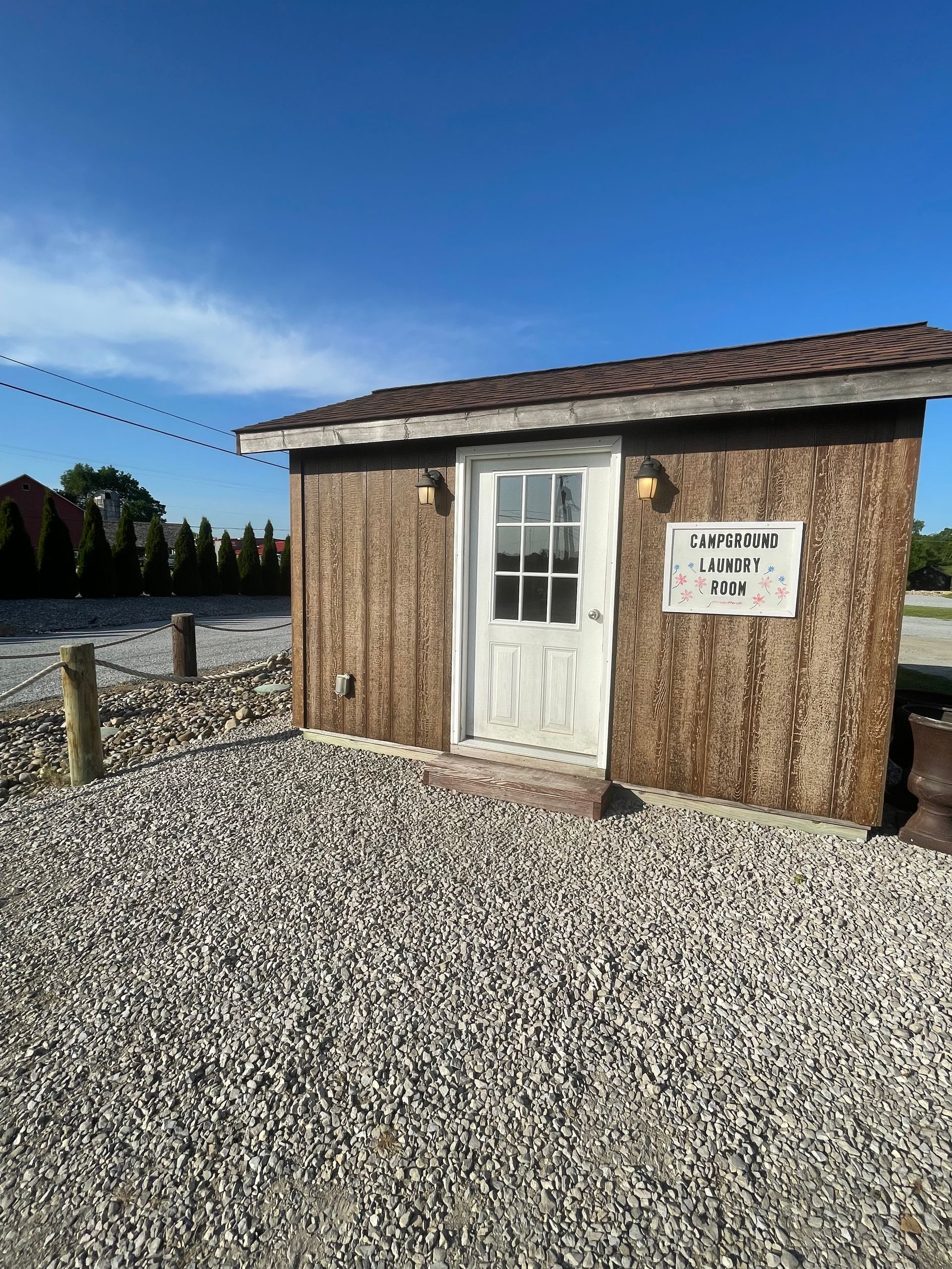 Small, weathered wooden shed with a white door and gravel ground under a blue sky.