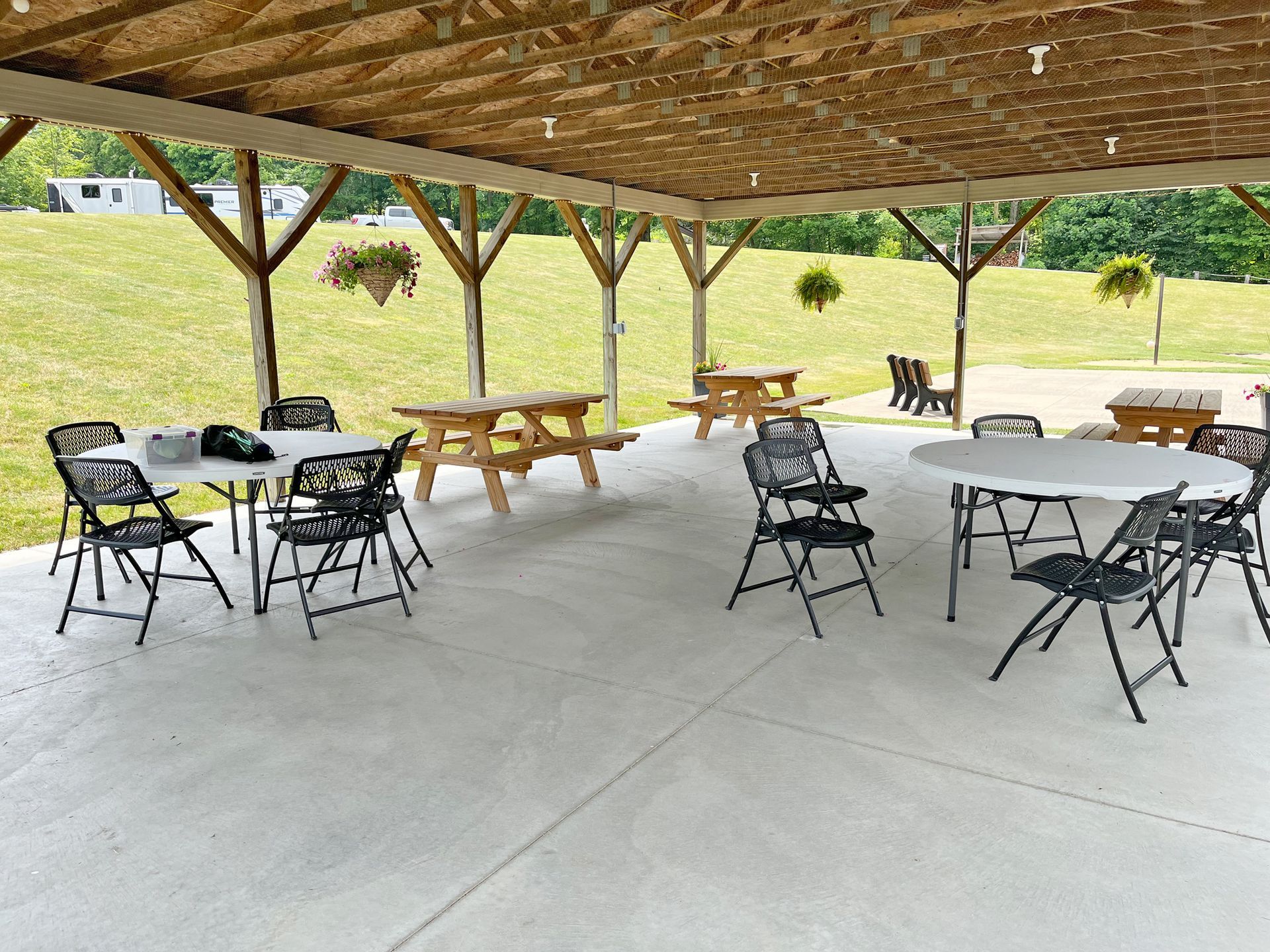 Pavilion with picnic tables and folding chairs; grassy hill in background.