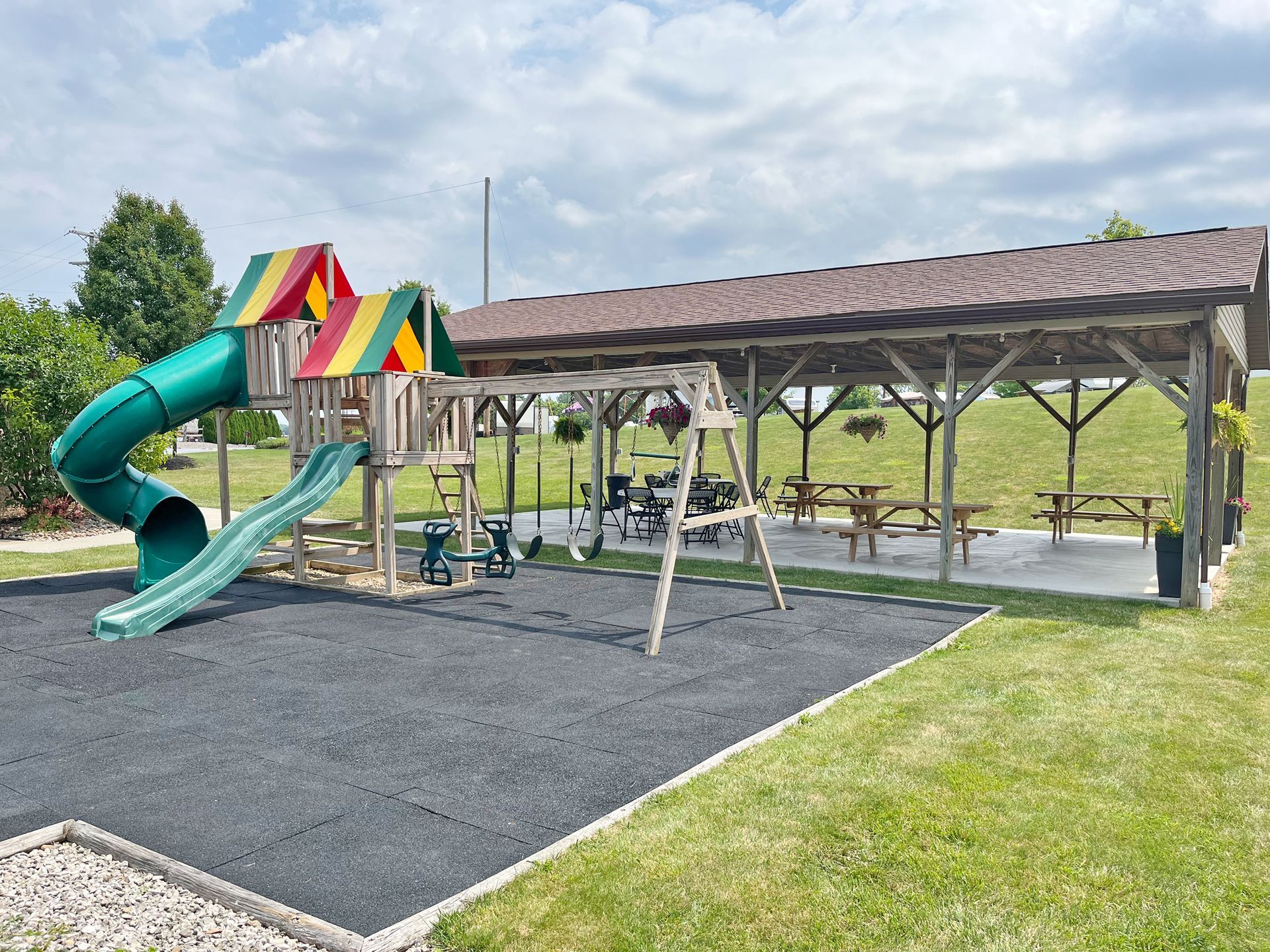 Playground with a slide, swings, and picnic tables under a covered shelter on a grassy area.