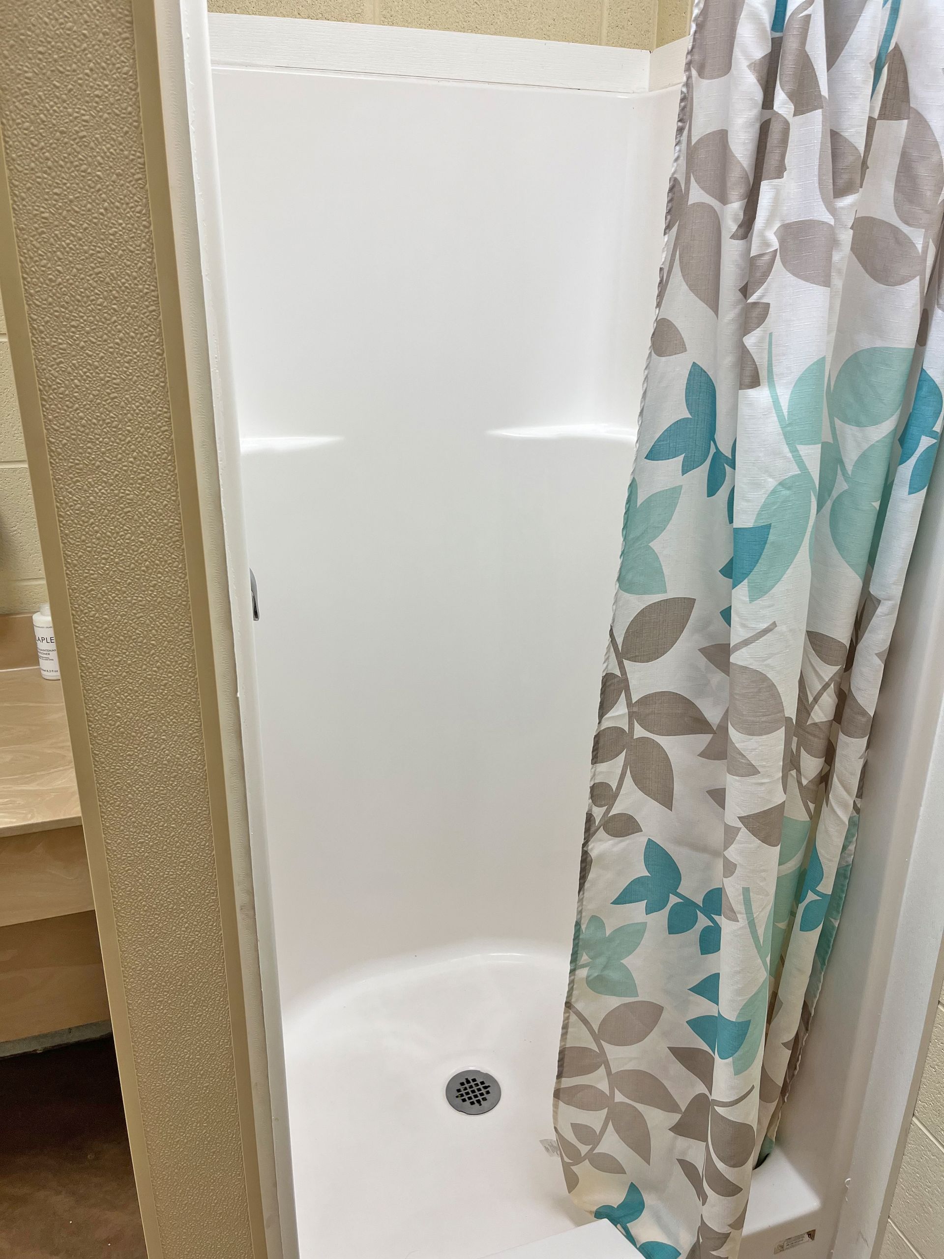 White, enclosed shower with floral shower curtain; beige walls.