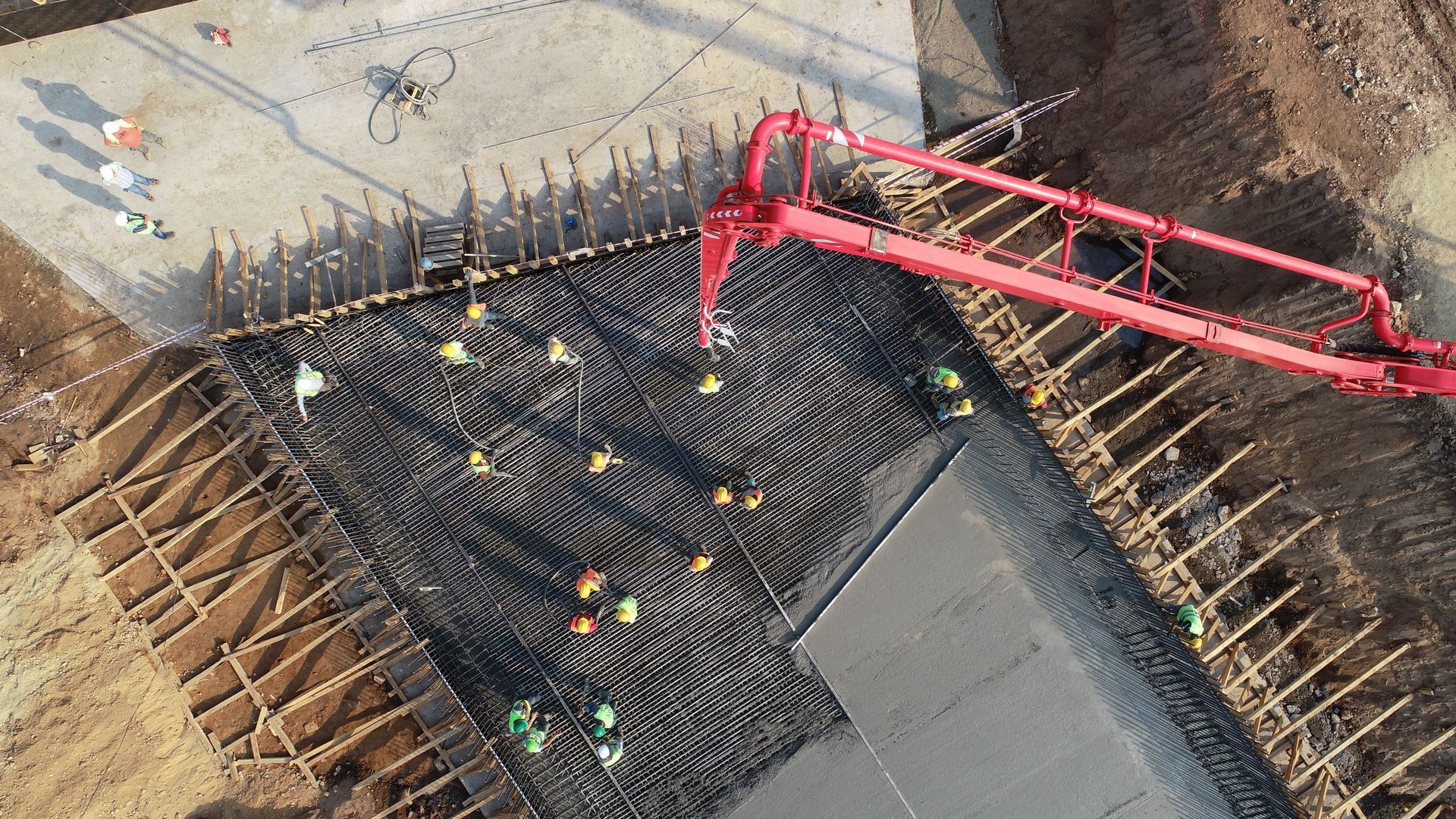 Overhead view of a construction site with a red concrete pump and workers around a rebar foundation.