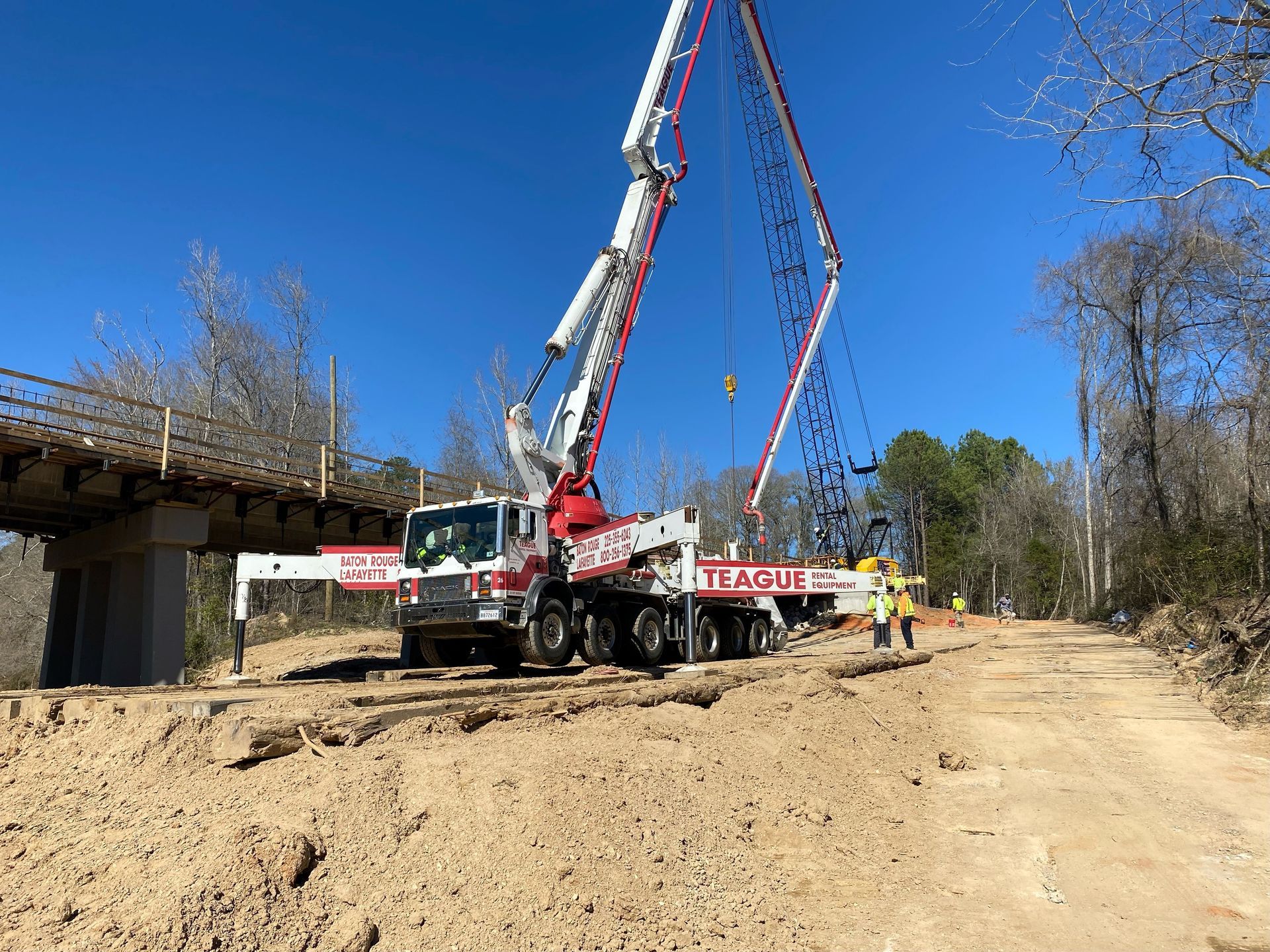 Concrete pump truck pouring concrete for a bridge construction on a dirt road. Blue sky.
