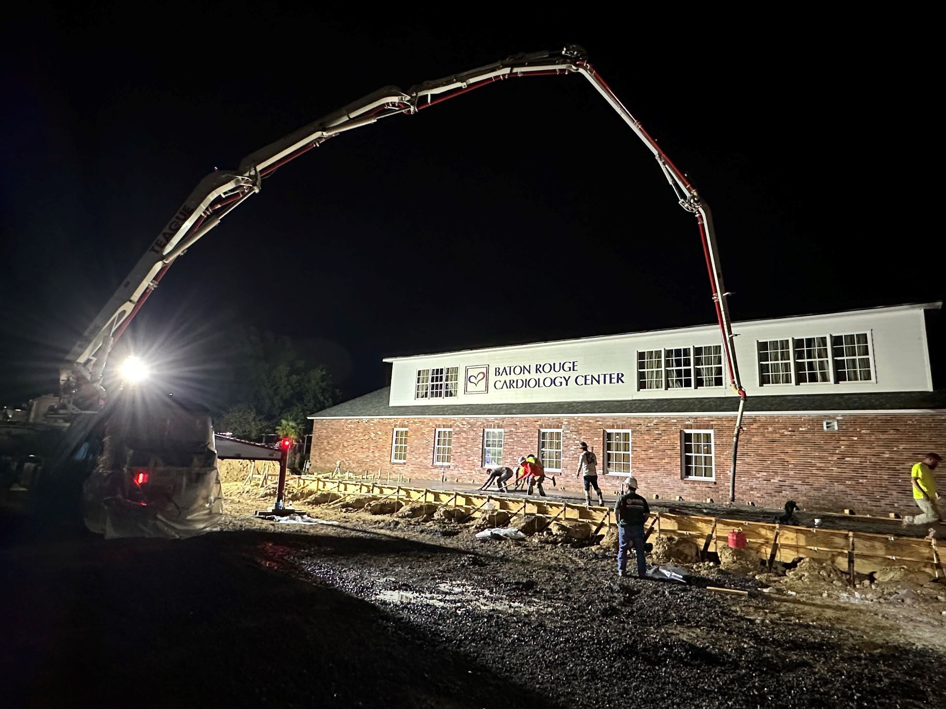 Construction workers pouring concrete at night. A long boom extends from a truck to the building.