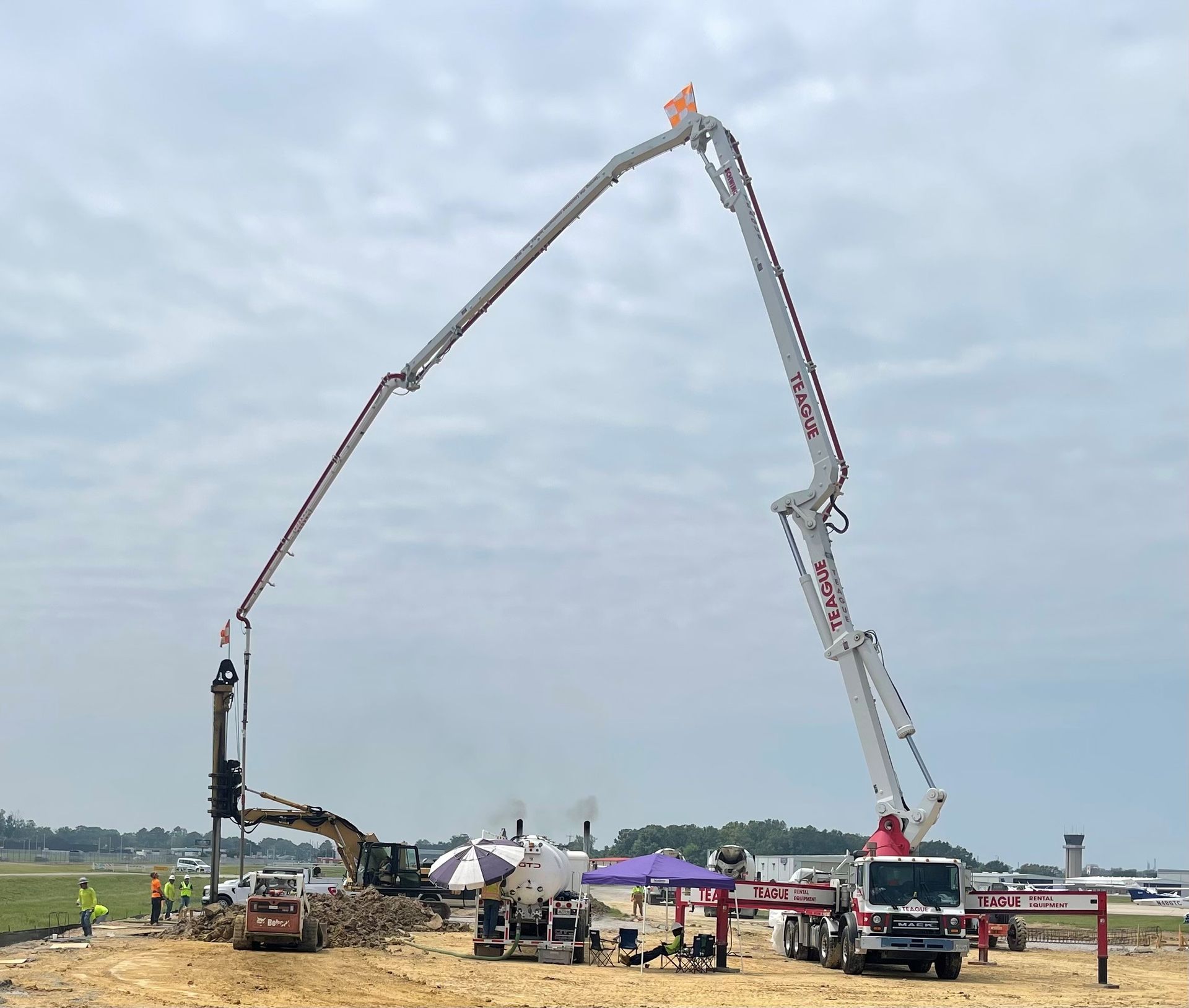 Concrete pump truck pouring concrete at a construction site near an airport.