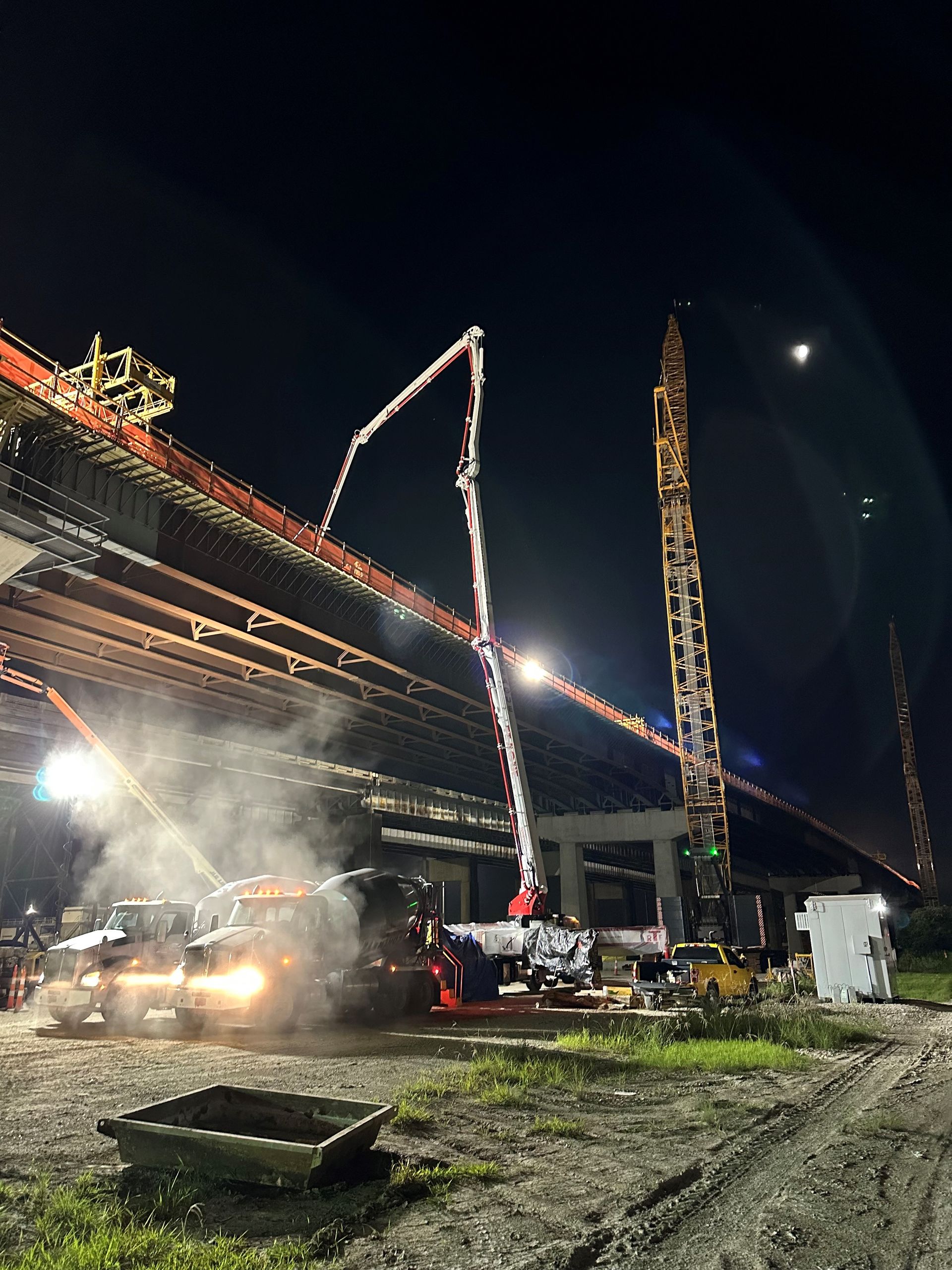 Construction site at night with concrete pumps pouring concrete for a bridge.