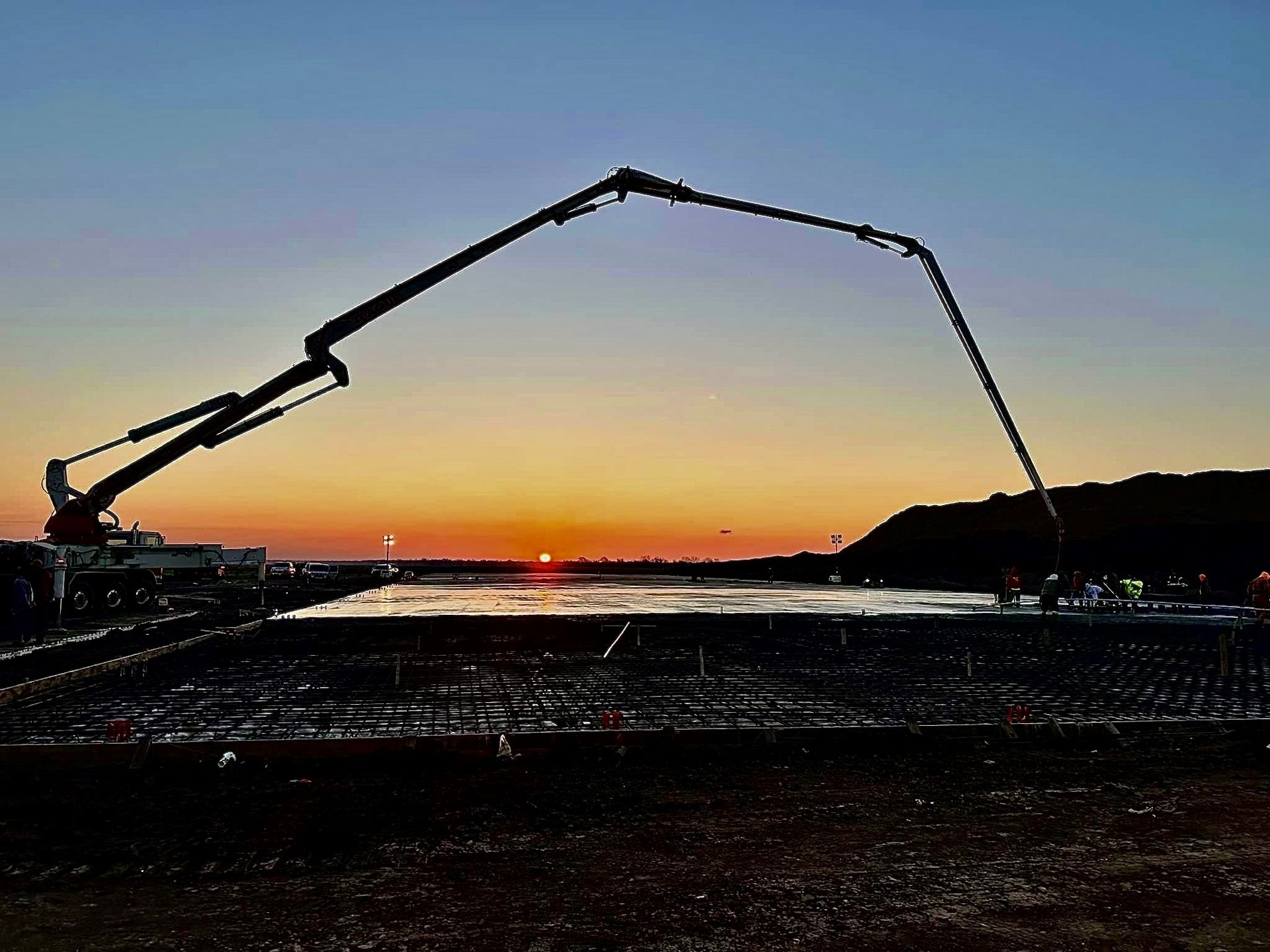 Concrete pump pours concrete at sunset over construction site.
