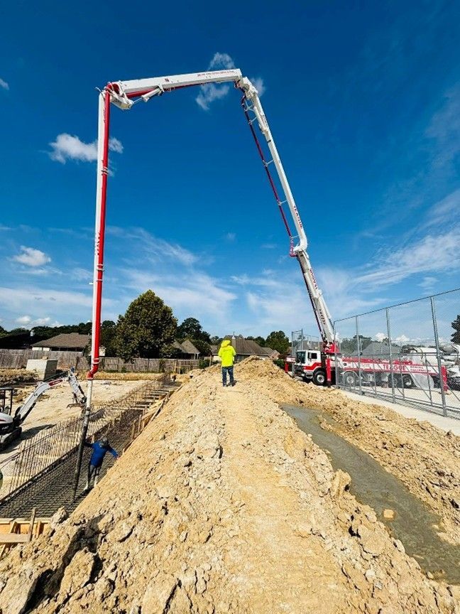 Construction site: concrete being poured from a boom pump onto a foundation. Workers are present.