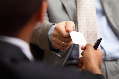 Two men in suits exchanging a business card and pen.