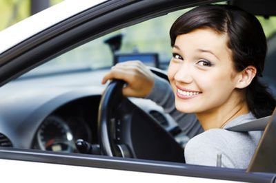 Woman smiling, driving a white car, looking at the camera.