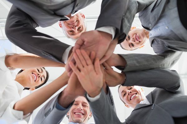 Group of business people with hands stacked together, celebrating a win, smiling, low-angle shot.