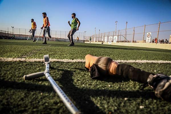 Soccer players with leg amputations practice on a field, crutch in foreground.