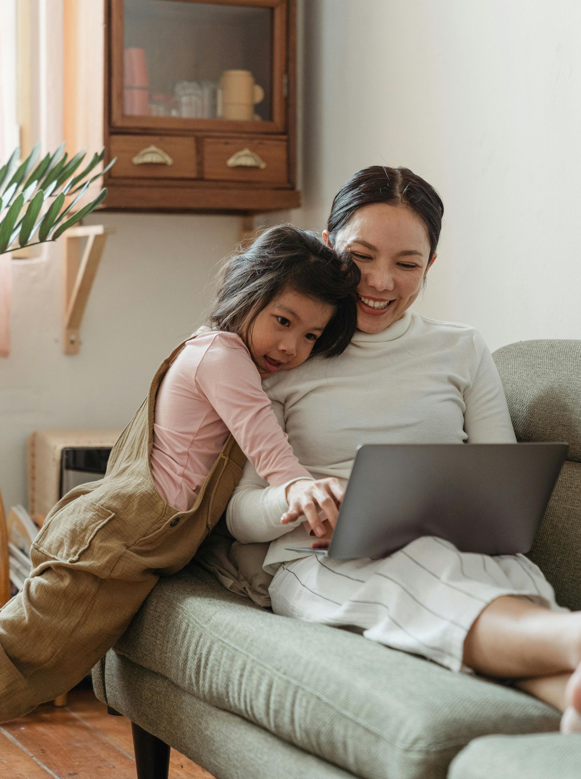Mother sitting on a couch with a laptop with her child at her side.