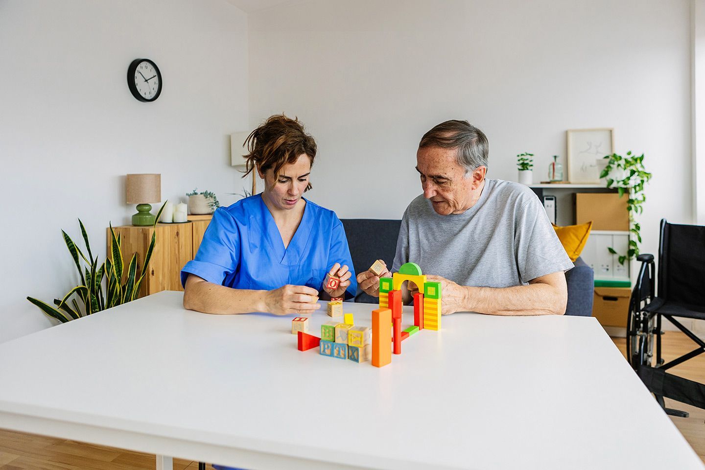 A healthcare worker and an older adult playing with colorful wooden blocks at a table.